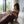 Load image into Gallery viewer, A person wearing a brown jumpsuit is sitting on a white couch and reading a book.