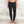 Charger l'image dans la galerie, A model wearing black high-waisted ankle-length leggings, standing barefoot against a textured light gray concrete wall.
