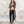 Load image into Gallery viewer, A woman stands barefoot against a textured light gray wall, wearing a long dark gray hooded zip-front cardigan draped over a gray sports bra and black leggings.
