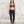 Charger l'image dans la galerie, A woman stands barefoot against a textured light gray wall, wearing a dark gray patterned sports bra and black leggings.
